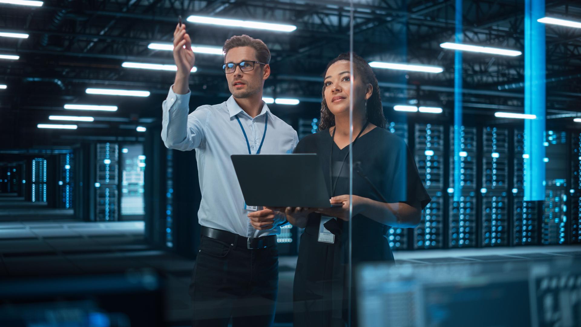 Information Technology Engineer and System Administrator Monitoring Web Services Cloud Solution Software and Sharing Ideas with Each Other in Big Data Center Server. People Use Laptop.